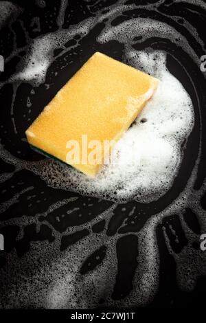 Primo piano della spugna gialla con sapone su superficie scura Foto Stock