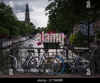 Biciclette e fiori su un ponte sul canale di Amsterdam in una giornata nuvolosa, i Paesi Bassi. Foto Stock