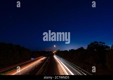 Sentieri luminosi sulla M6 con la Luna in lontananza Foto Stock