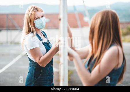 Madre e figlia in piedi su lati diversi di recinzione indossare maschere mediche che si guardano l'un l'altro. Concetto di allontanamento sociale Foto Stock