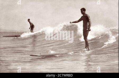 Due surfisti che cavalcano tavole da surf in legno a Waikiki a Honolulu, territorio delle Hawaii negli anni '30. Foto Stock