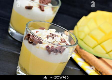 Budino di frutta di mango in un vaso di bicchieri e cubetti di mango su tavolo di legno nero Foto Stock