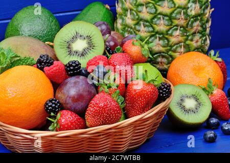 Un cestino su un tavolo di legno blu contiene un mucchio di frutta e bacche diverse Foto Stock