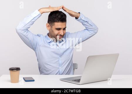 Assicurazione di sicurezza, vita garantita. Agente uomo positivo seduto in ufficio, parlando con il cliente in videochiamata e mostrando il gesto del tetto della casa sopra l'hea Foto Stock