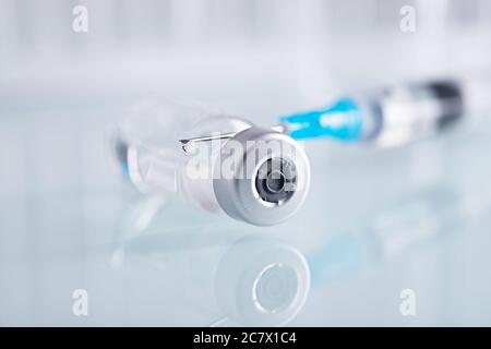 Shot di chiusura di una siringa e di un flaconcino di vetro chiuso con liquido trasparente su una superficie bianca Foto Stock