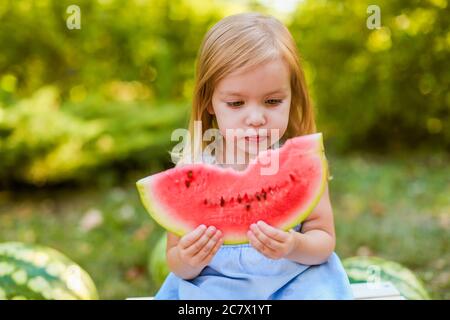 Bambino che mangia cocomero in giardino. I bambini mangiano frutta all'aperto. Snack sano per i bambini. ragazza di 2 anni che gode anguria Foto Stock