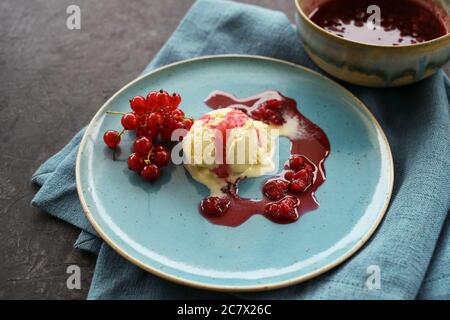 Gelato alla vaniglia con ribes rosso e salsa di gelatina di frutta su un piatto blu, tovagliolo e sfondo scuro con spazio di copia, fuoco selezionato, profondità ridotta di Foto Stock