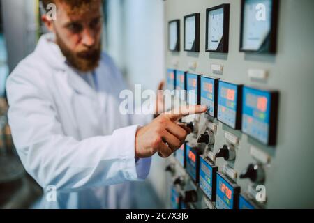 Operatore di quadri di controllo macchina in impianto di produzione. Specialista tecnico caucasico in tuta bianca che lavora in fabbrica di alimenti e bevande Foto Stock