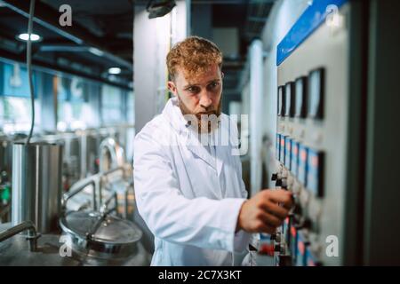 Operatore di quadri di controllo macchina in impianto di produzione. Specialista tecnico caucasico in tuta bianca che lavora in fabbrica di alimenti e bevande Foto Stock