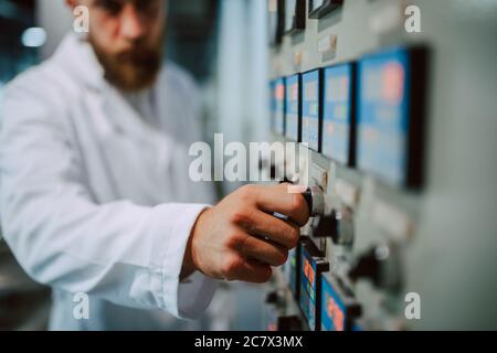 Operatore di quadri di controllo macchina in impianto di produzione. Specialista tecnico caucasico in tuta bianca che lavora in fabbrica di alimenti e bevande Foto Stock