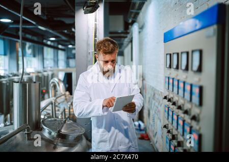 Professionista caucasico bel tecnologo in bianco uniforme standing in fabbrica farmaceutica o alimentare - produzione di controllo impianti Foto Stock