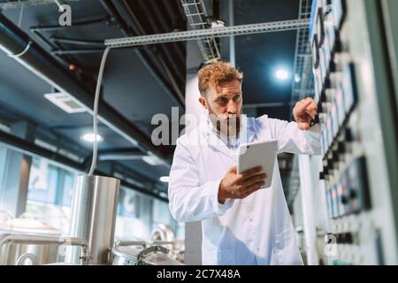 Professionista caucasico bel tecnologo in bianco uniforme standing in fabbrica farmaceutica o alimentare - produzione di controllo impianti Foto Stock