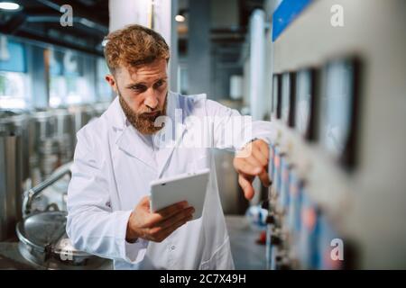 Professionista caucasico bel tecnologo in bianco uniforme standing in fabbrica farmaceutica o alimentare - produzione di controllo impianti Foto Stock