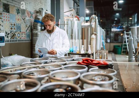 Professionista caucasico bel tecnologo in bianco uniforme standing in fabbrica farmaceutica o alimentare - produzione di controllo impianti Foto Stock