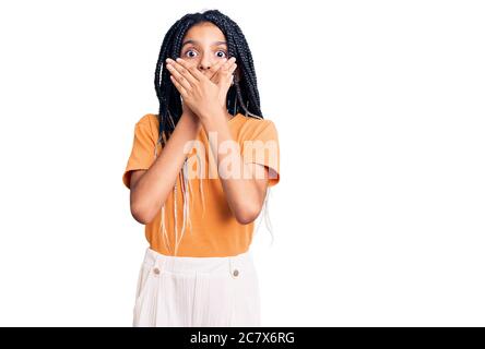 Carino african american ragazza indossando abiti casual scioccato coprendo la bocca con le mani per errore. Concetto segreto. Foto Stock