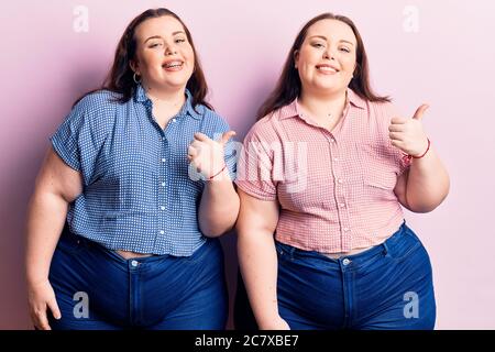 I gemelli più piccoli indossano abiti casual che puntano alla parte posteriore dietro con mano e pollici in su, sorridendo sicuro Foto Stock