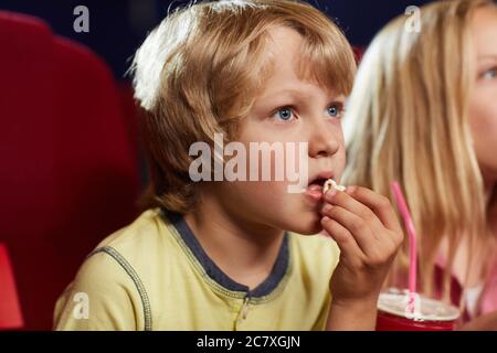 Ritratto di un ragazzo biondo che guarda il film in cinema e mangiare popcorn, copia spazio Foto Stock