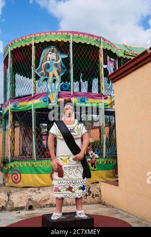 Vecchio e nuovo. Una statua di una donna in abito tipico tradizionale a Santa Elena, Yucatan, Messico. Dietro di lei è un personaggio moderno cartone animato ragazza. Foto Stock