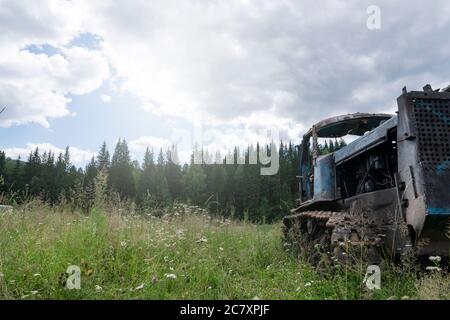 Un vecchio trattore cingolato arrugginito, abbandonato in un campo, sullo sfondo di una pineta in Siberia. Declino e crollo dell'agricoltura in Russia. Foto Stock