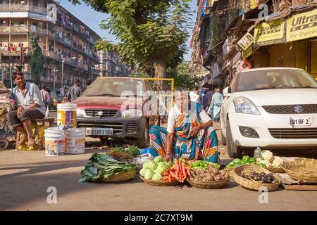 Una venditrice di verdura femminile nella trafficata zona di Bhendi Bazar a Mumbai, India, ha distribuito i suoi articoli in cestini sul lato della strada Foto Stock