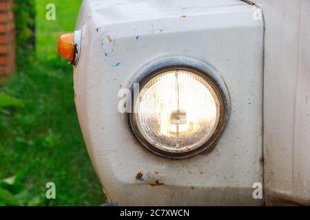 Primo piano del faro di un vecchio camion abbandonato con pannelli bianchi arrugginiti Foto Stock