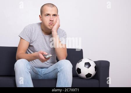 tifoso di calcio annoiato con la palla che guarda la partita in tv a casa Foto Stock