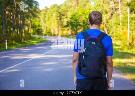 hitchhiking concetto - vista posteriore di uomo con zaino che cammina sulla strada forestale Foto Stock