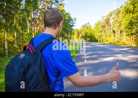 hitchhiking concetto - uomo con zaino in piedi su strada forestale Foto Stock