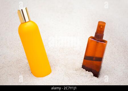 concetto di solarium - primo piano di crema solare e bottiglie spray sulla spiaggia di sabbia Foto Stock