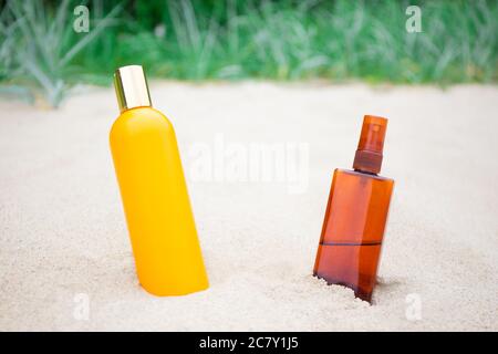 concetto estivo e di cura della pelle - lozione e spruzzatori di sole su spiaggia sabbiosa Foto Stock