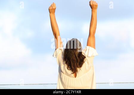 Indietro vista ritratto di una donna adulta eccitata che celebra il successo alzando le braccia in piedi su un balcone Foto Stock