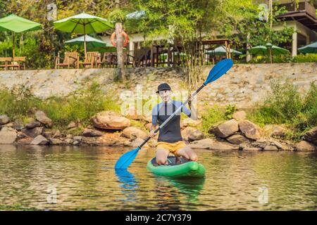 L'uomo gioioso sta addestrando il bordo del SUP nel fiume in una mattina soleggiata. Stand up paddle boarding - attività ricreative all'aperto impressionante Foto Stock