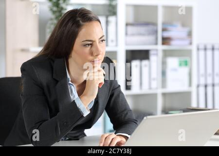 Donna esecutiva pensante che guarda awaywith laptop seduto sulla sua scrivania in ufficio Foto Stock