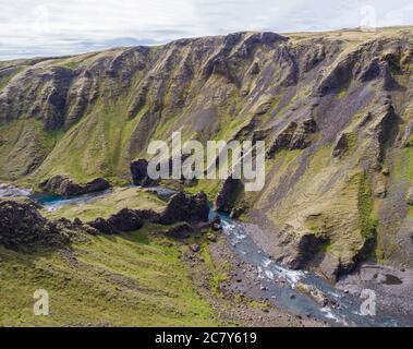 Vista sul torrente del fiume e le scogliere coperte di muschio verde e le colline nella gola di Eldgja in Islanda, la riva d'erba, cielo blu Foto Stock