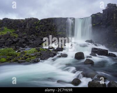 Cascata di Oxarfoss nella riserva naturale di Thingvellir Islanda con rocce vulcaniche e muschio, che cade dalla fessura nel crinale medio-Atlantico, lunga esposizione Foto Stock