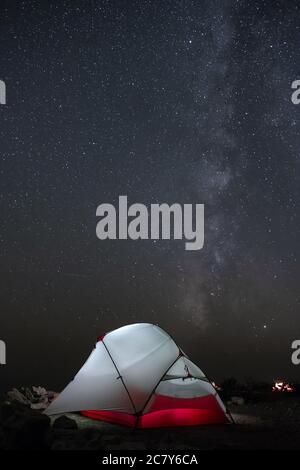 Una tenda si illumina sotto un cielo notturno pieno di stelle. Foto Stock