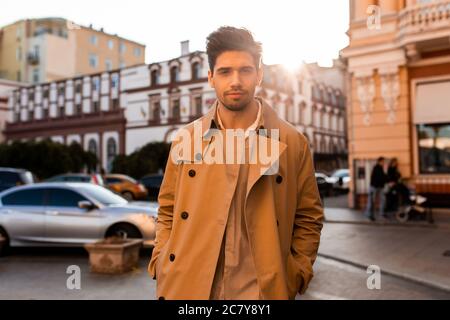 Giovane uomo casual bello in trench cappotto guardando con sicurezza in macchina fotografica su strada Foto Stock
