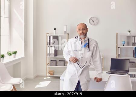 Un medico praticante è di mezza età con i bicchieri nei fiumi in piedi nella clinica. Foto Stock