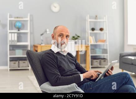 Uomo maturo con un computer tablet che lavora online, che parla con la famiglia, che consulta un medico o guarda un webinar a casa Foto Stock