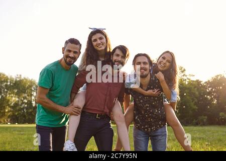 Gruppo di amici felici cavalcare in piggyback ridendo abbracciando la natura in estate in primavera. Foto Stock