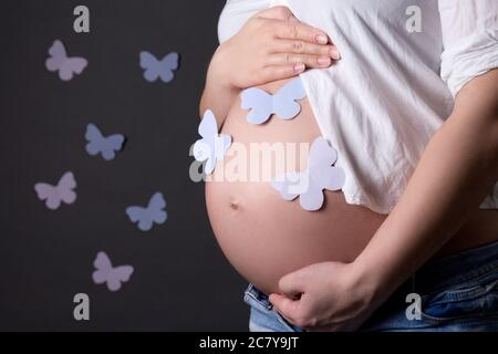 ventre di donna incinta con farfalle colorate su sfondo grigio Foto Stock