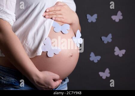 ventre donna incinta con farfalle colorate di carta su sfondo grigio Foto Stock