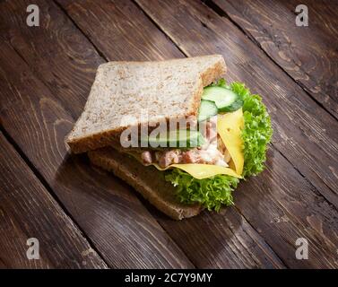 chiocciolato di panino di tonno con foglie di lattuga verde, formaggio, uova tritate, cetrioli e pane di segala o di frumento, su sfondo di legno rustico scuro, no Foto Stock