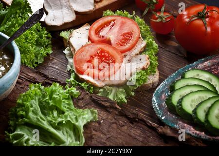 sandwich di carne di tacchino con pomodori freschi, insalata di lattuga verde e cetrioli su sfondo rustico di legno scuro, nessuno Foto Stock