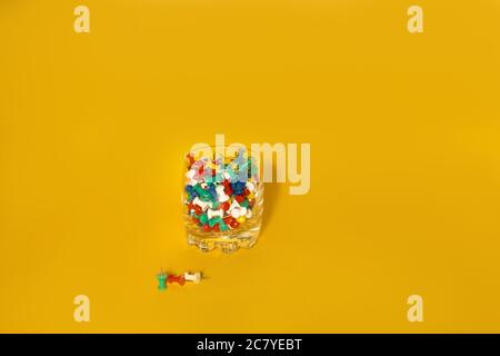 Immagine in primo piano di piccoli pulsanti colorati per ufficio sul vetro con sfondo giallo Foto Stock