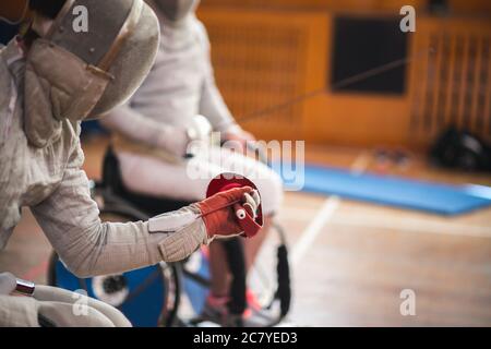 Primo piano di uomo finitore si abbatti indossando costume bianco scherma e tenendo la sua maschera scherma e una spada su sfondo soleggiato Foto Stock