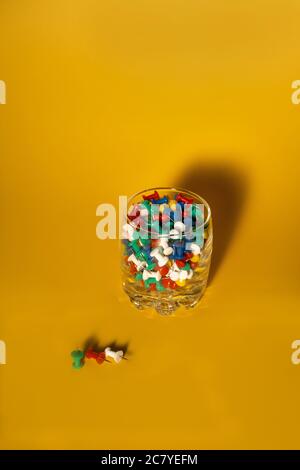 Immagine in primo piano di piccoli pulsanti colorati per ufficio sul vetro con sfondo giallo Foto Stock