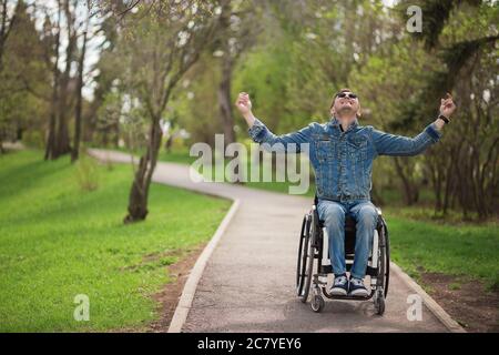 mano maschile sulla ruota della sedia a rotelle durante la passeggiata nel parco Foto Stock