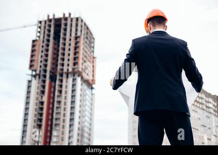 Ritratto di un architetto costruttore che studia la pianta delle stanze, serio ingegnere civile che lavora con documenti sul cantiere, costruzione e h Foto Stock