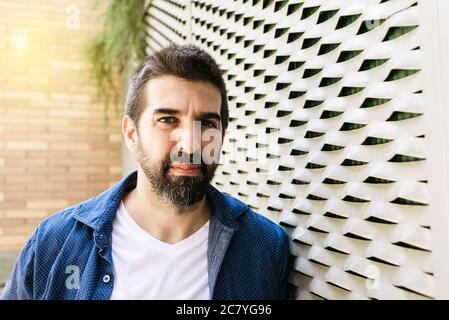 Maschio con cuscinetti pensierosi appoggiato sulla parete con la mano sul mento Foto Stock